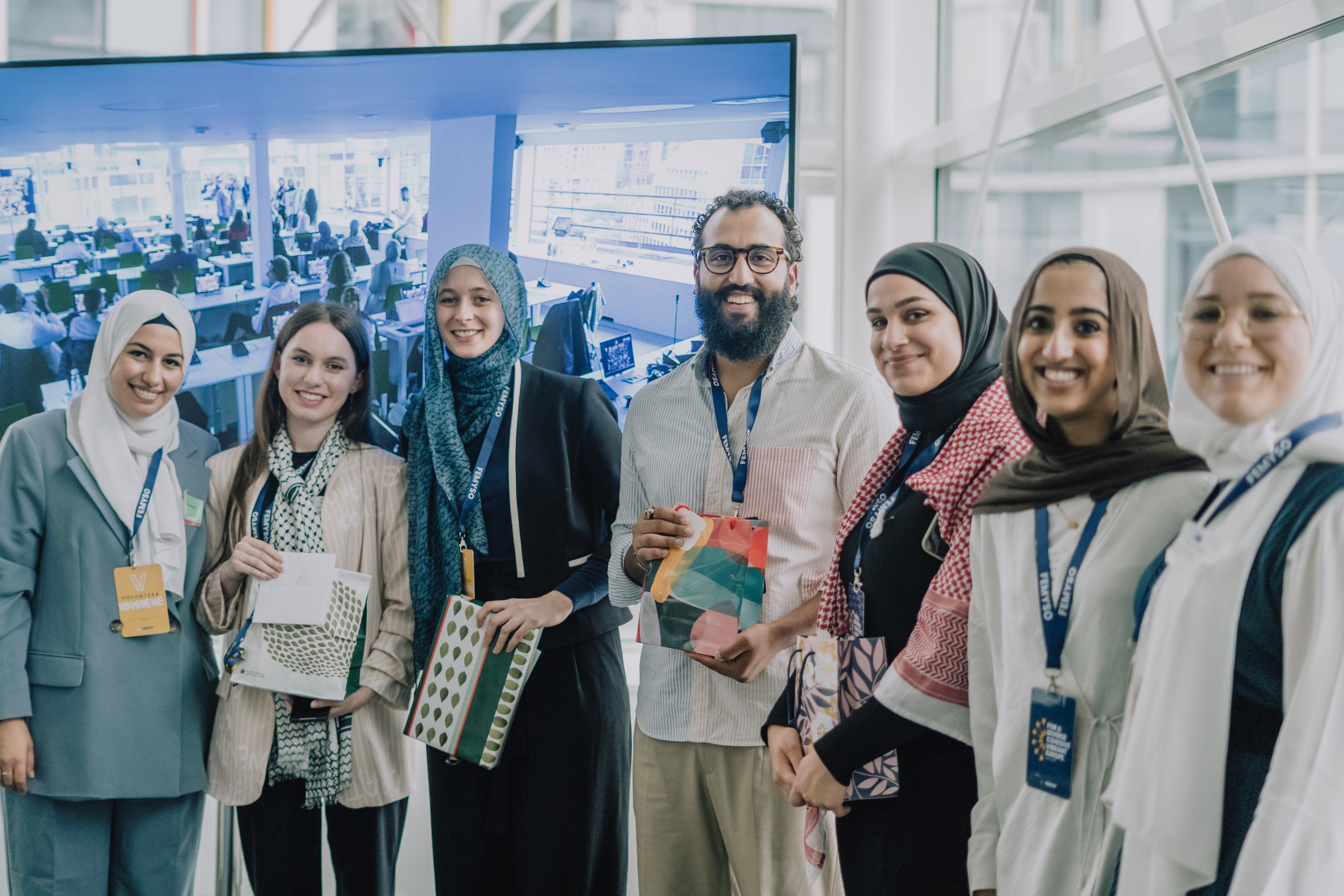 A group of young Muslim women and a man stand smiling at the camera, with lanyards around their necks.